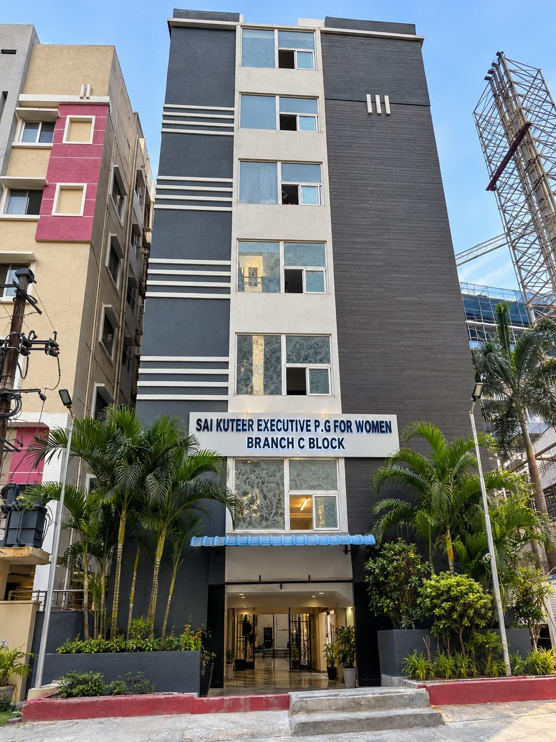 Inovies Street women's block, a tall charcoal-grey building with a Sai Kuteer name board above a landscaped entrance lined with palms